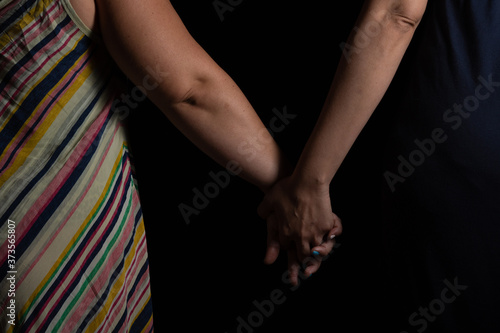 Young lesbian couple holding hands in studio with black background