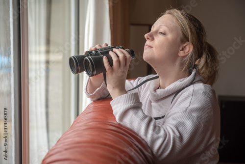 Fotografie Women in late twenties spying with binoculars through s window