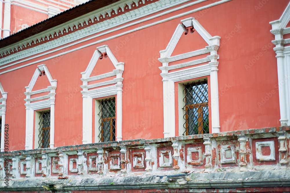 Obraz premium Pale red wall of the Russian church with white windows and metal bars.Decoration of the old building.