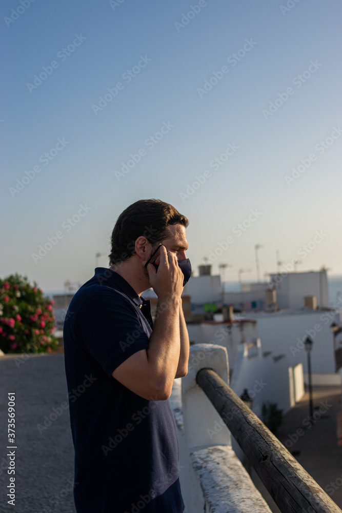 Obraz premium Photo of a young and attractive man wearing a face mask enjoying the views of Conil. White houses, doing tourism during coronavirus outbreak. Social distance and isolation