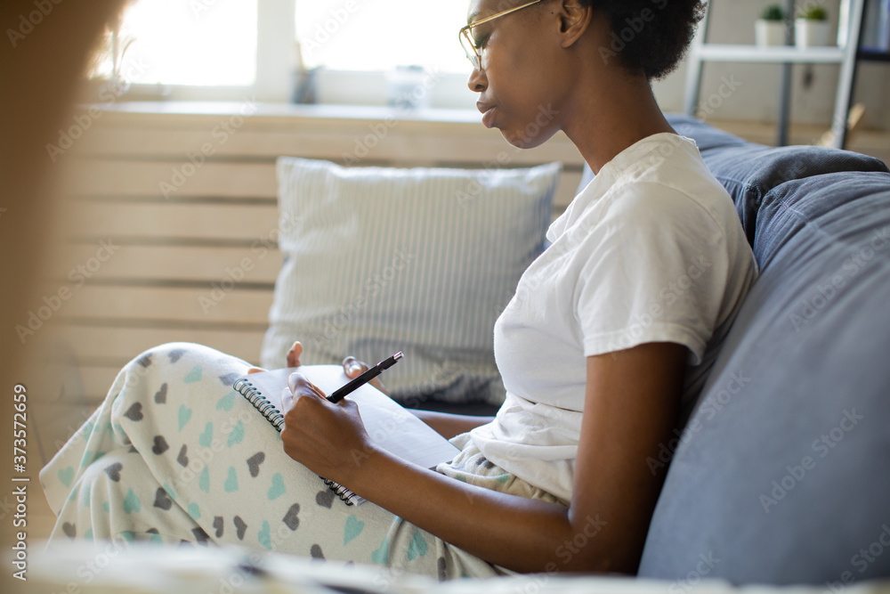 African American girl writes in a notebook in a cozy room African American girl writes in a notebook in a cozy room