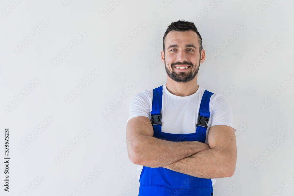 A repairman in a work clothes stands with folded arms on his chest