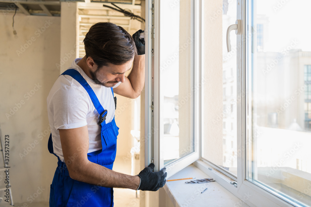 Workman in overalls and gloves checks the window frame Workman in overalls and gloves checks the window frame