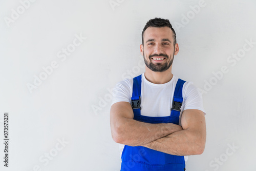 A repairman in a work clothes stands with folded arms on his chest