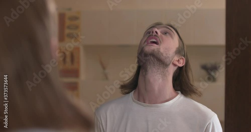 Young man stands in front of a mirror, gargle throat and spit out water