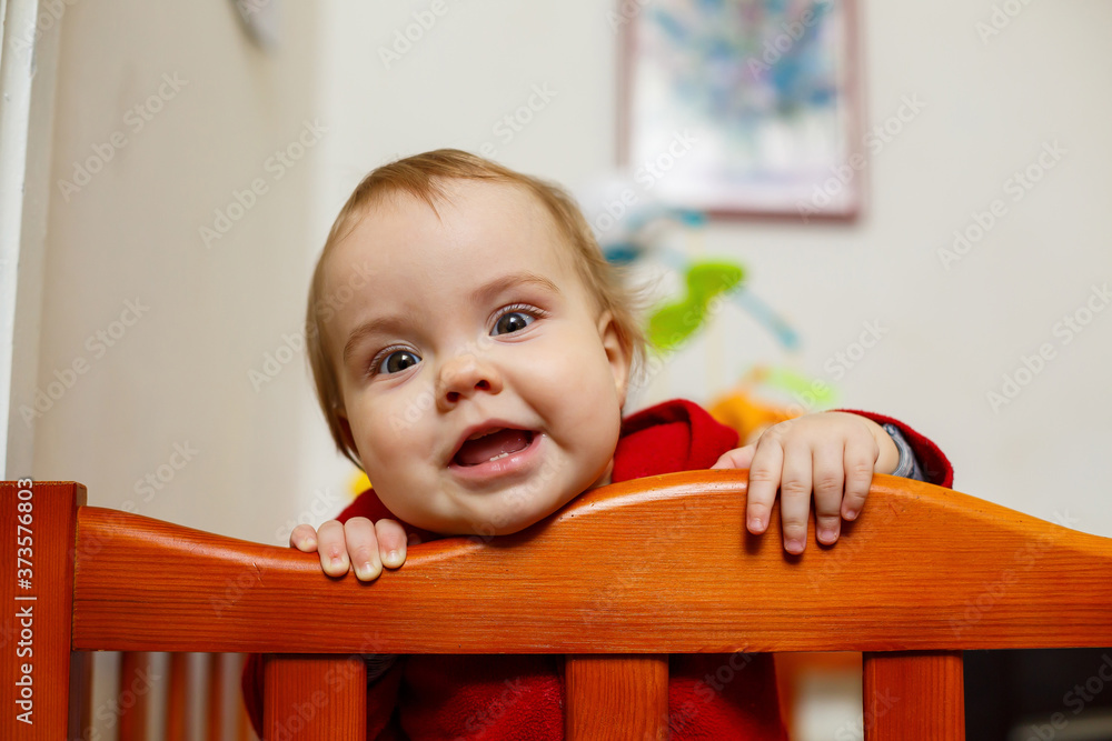 little child girl in a red sweater, smiles beautifully, in a crib, plays and has fun, emotional photo little child girl in a red sweater, smiles beautifully, in a crib, plays and has fun, emotional photo