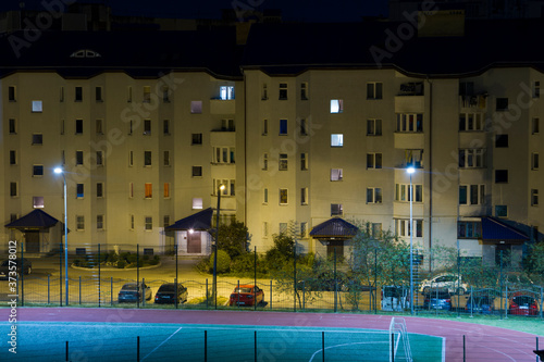 Low-rise residential building illuminated by lanterns at night. Soccer field and running track at night.
