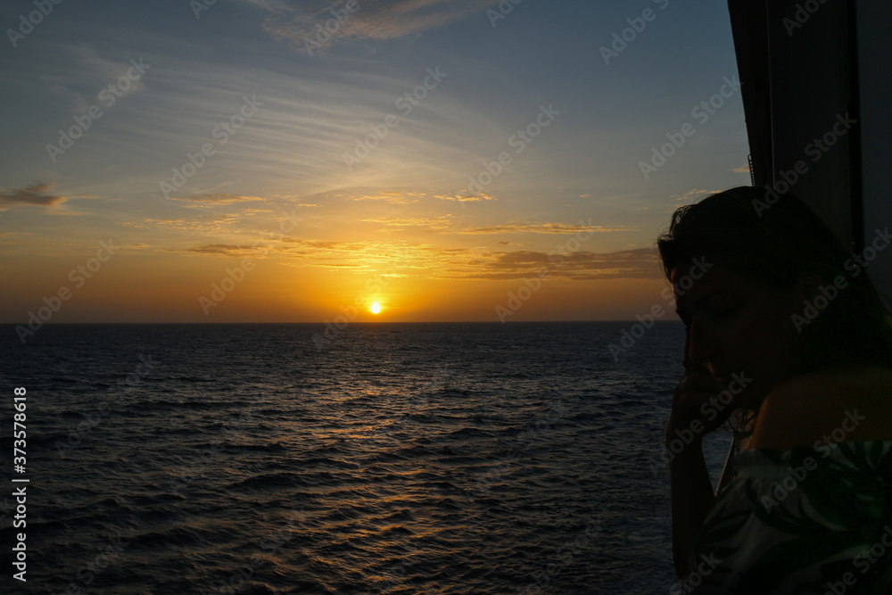 Silhouette of a woman on a cruise ship desk with sunset in the background