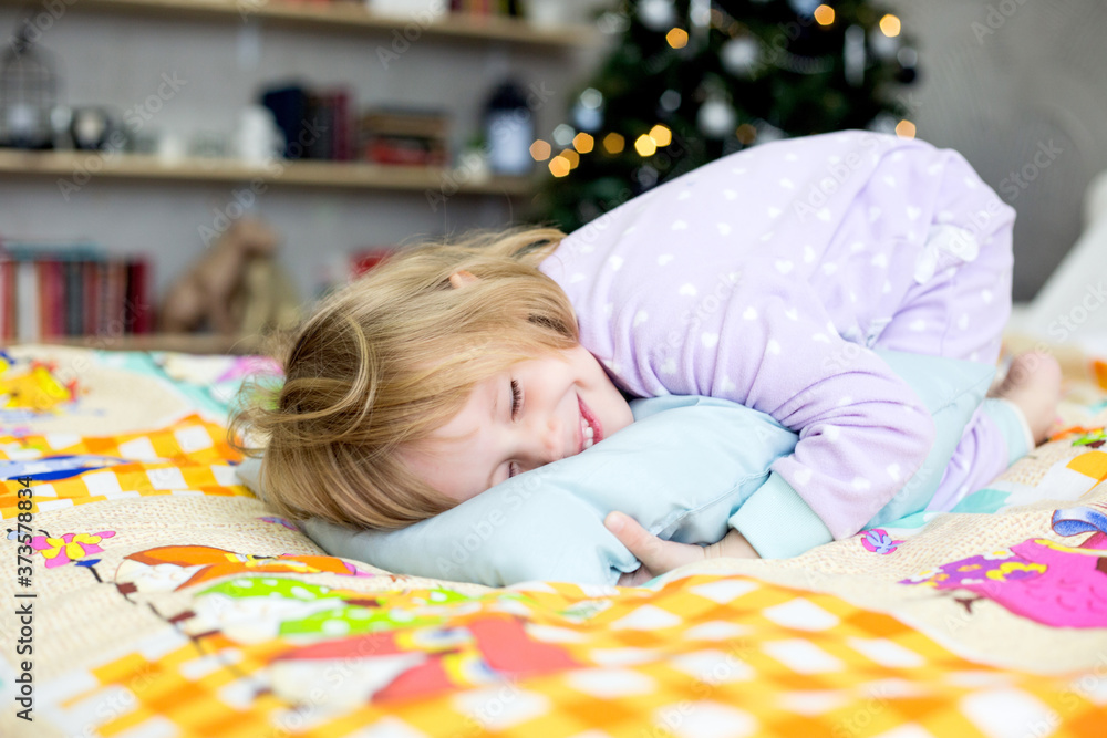christmas morning,a little girl in pajamas is lying in bed and hugging a pillow christmas morning,a little girl in pajamas is lying in bed and hugging a pillow
