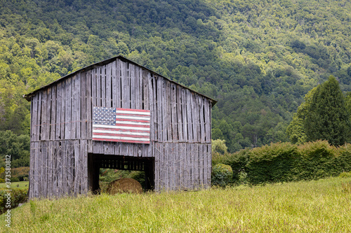 Fotomurale An old barn with an American flag painted somewhere in the mountains on a sunny