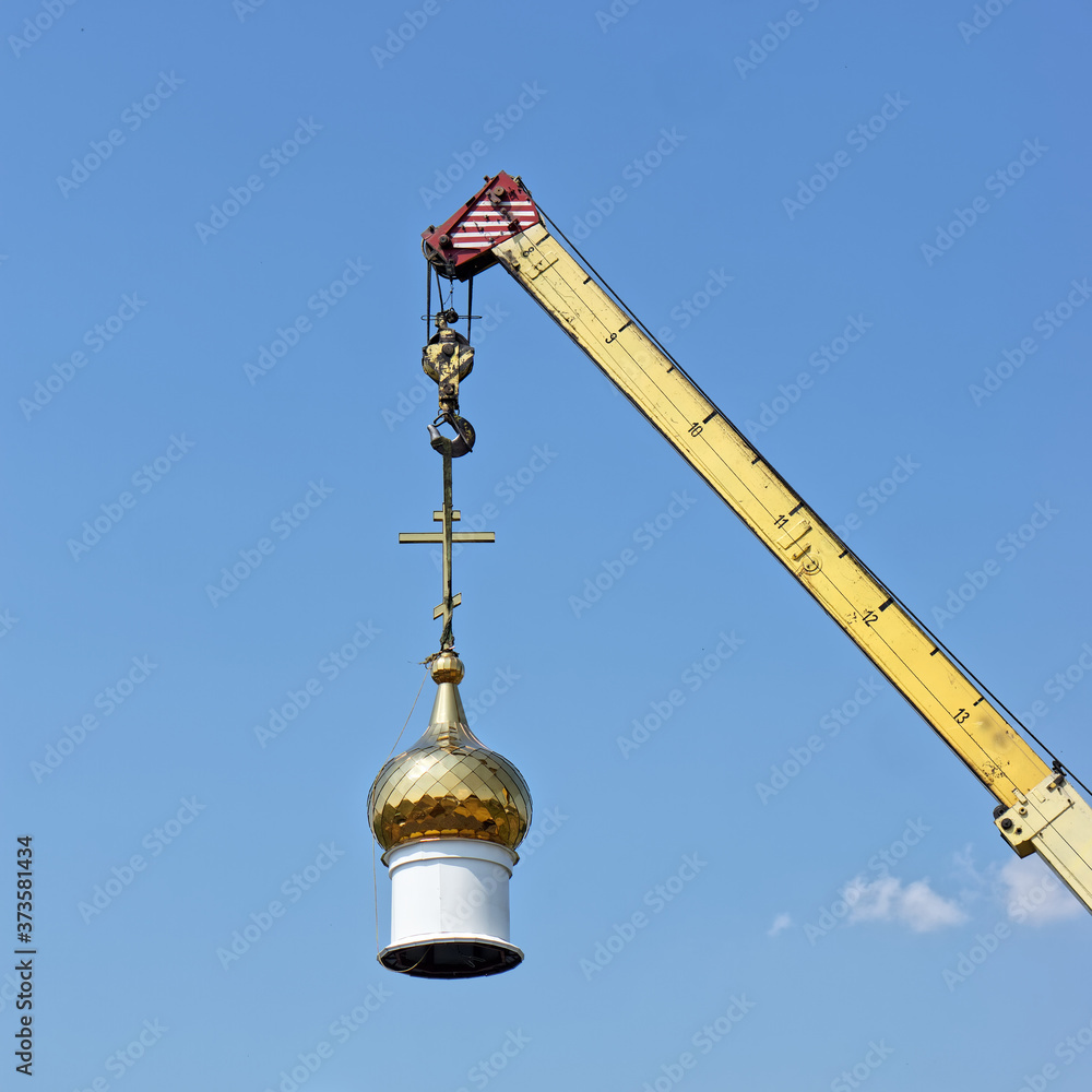 The dome of a Christian temple hangs on the hook of a crane. Building or dismantling a church against a blue sky