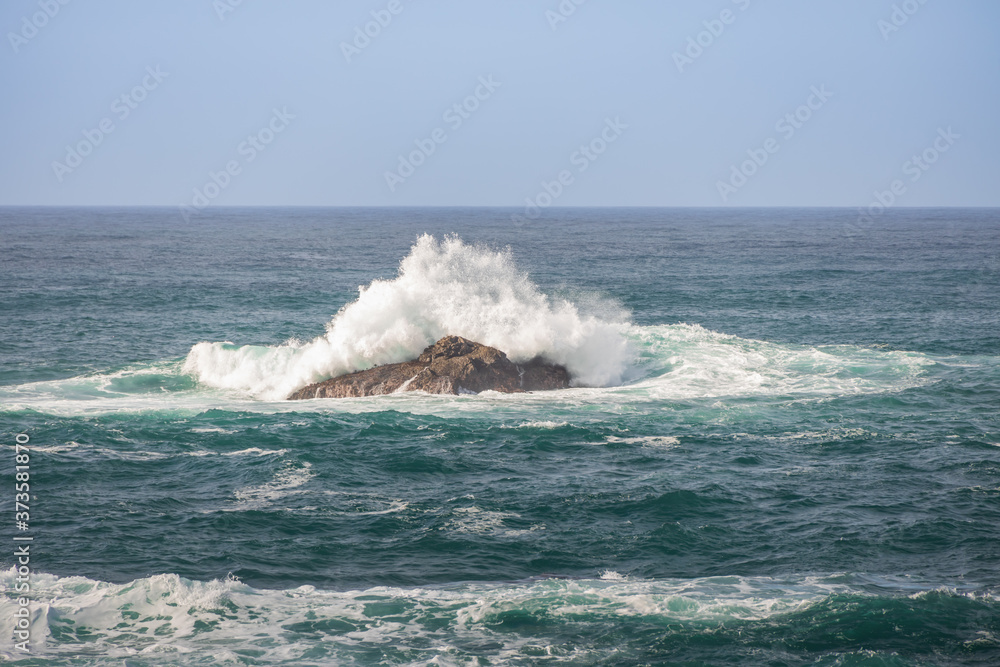 Fototapeta premium Waves breaking on large rock in ocean