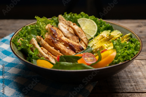 Grilled chicken salad with avocado and vegetables on wooden background