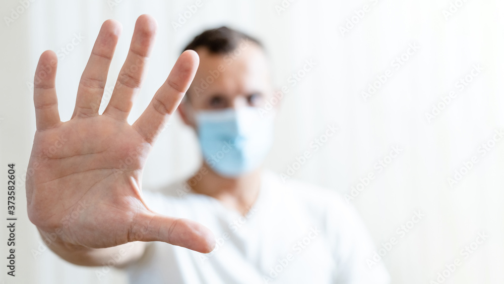 blurred man in medical mask shows open palm stop gesture on light background with copy space blurred man in medical mask shows open palm stop gesture on light background with copy space