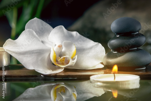 Black zen stones candles and white orchids on a wooden plank on the surface of the water. SPA  relaxation  meditation concept