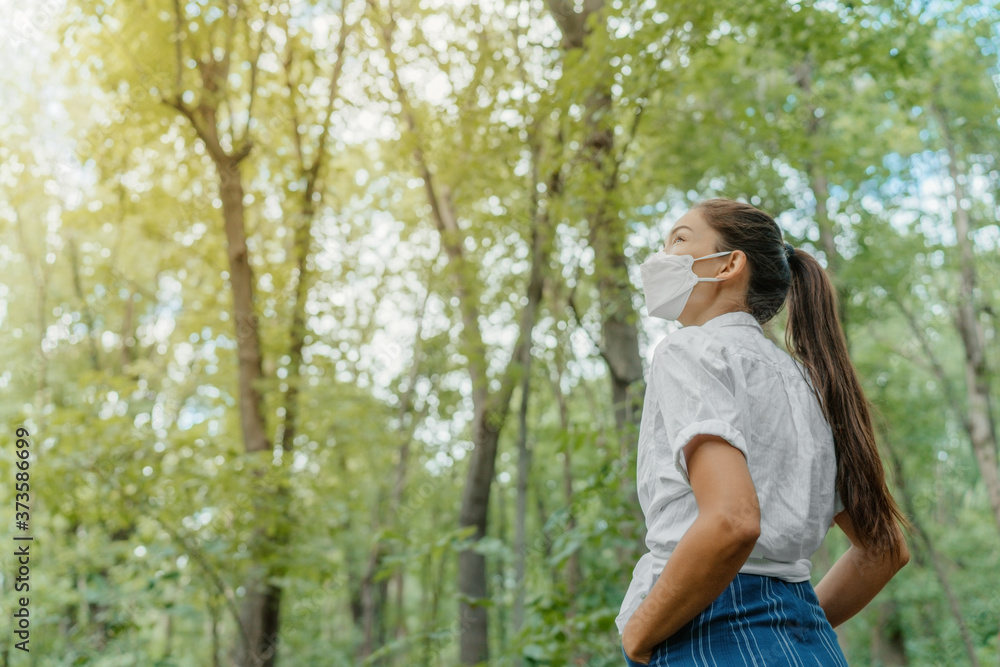 Eco-friendly sustainable face mask. Woman wearing kn95 korean masks walking in outdoor forest lookin up at sunlight. Hope concept for environment. Coronavirus covering. Eco-friendly sustainable face mask. Woman wearing kn95 korean masks walking in outdoor forest lookin up at sunlight. Hope concept for environment. Coronavirus covering.
