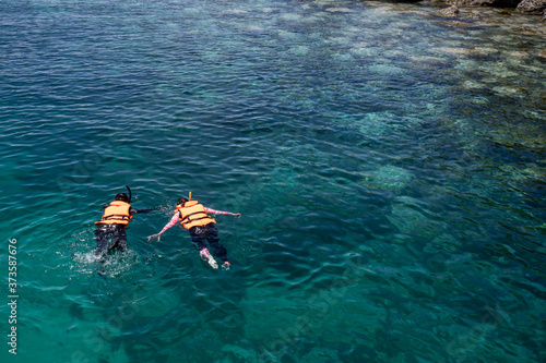 Two people snorkeling wear a life jacket over coral reef with clear blue ocean water in tropical clear sea