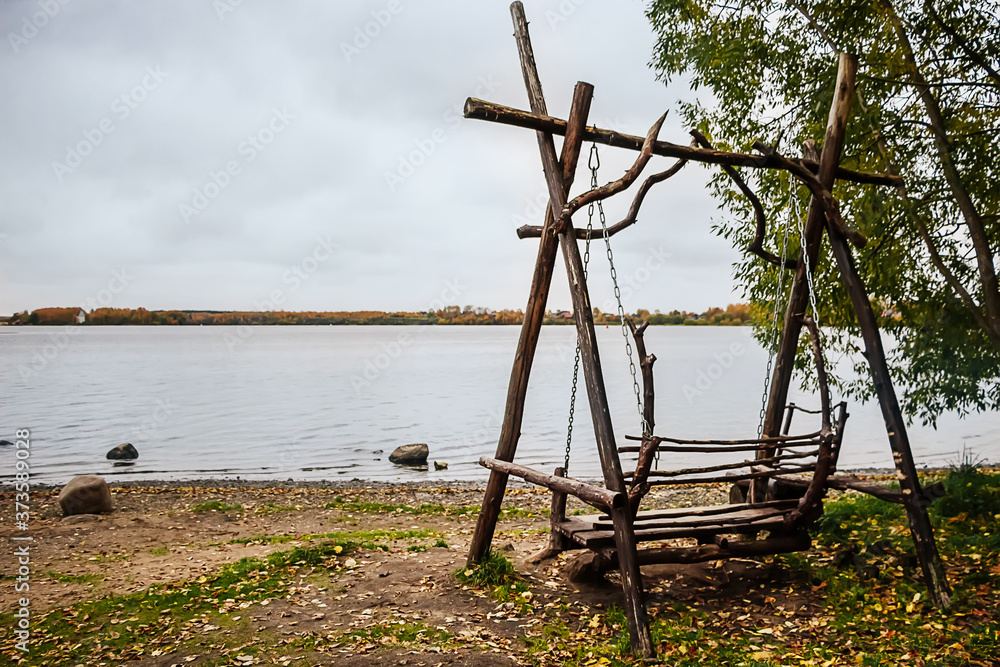 Wooden swing on lake by autumn cloudy day