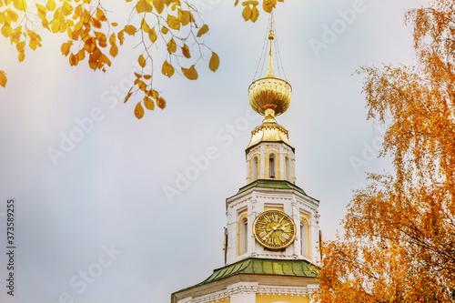 Ancient christian church and autumn yellow trees. Beautiful domes, high old bell tower against the sky
