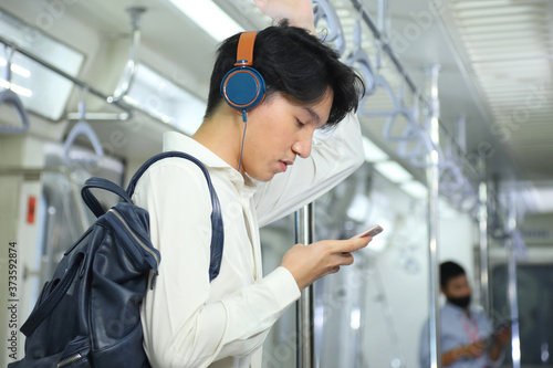 A lifestyle of young Asian man using cellphone with headset while taking the subway train to work at the rush hour morning with copy space