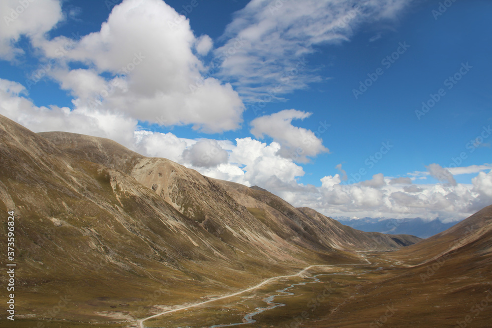 View of mountains, dirt road and stream with the dramatic sky in Tibet, China