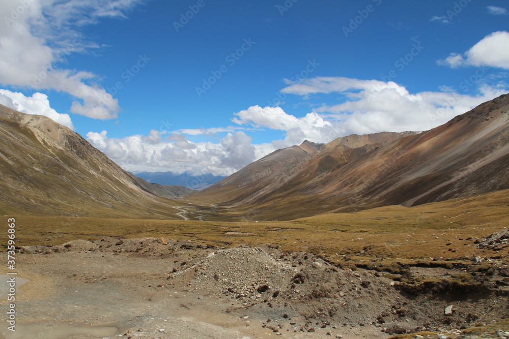 View of mountains and dirt road with the dramatic sky in Tibet, China