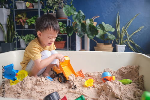 Cute Asian young boy playing with sand alone at home, Kid playing with sand toys & toy construction machinery in urban home garden , Montessori education, Creative play for kids concept