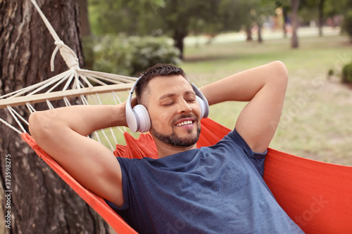 Handsome man listening to music while relaxing in hammock outdoors