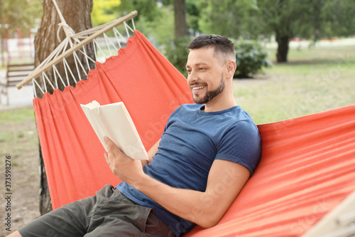 Handsome man reading book while relaxing in hammock outdoors