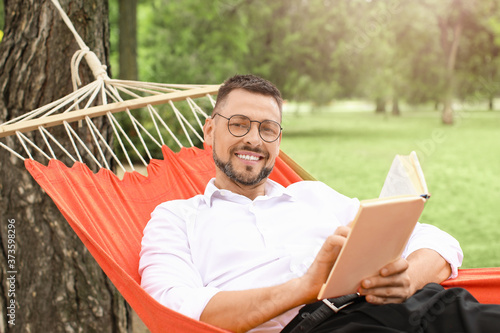 Handsome businessman reading book while relaxing in hammock outdoors