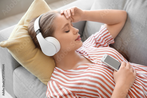 Sleepy young woman listenin...