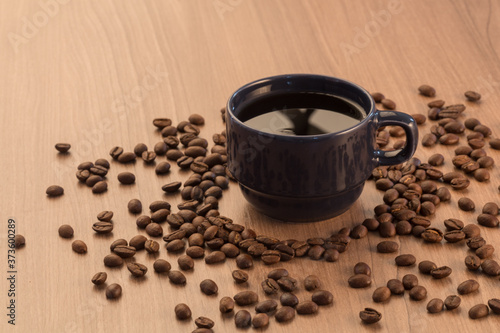 blue mug with black coffee, with coffee bean around it, on a flat wooden surface