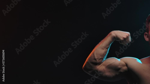 Muscular athlete flex biceps on arm, showing muscles. Concept of sports and body. Shot in the studio on a black background. Slow motion. Close up.