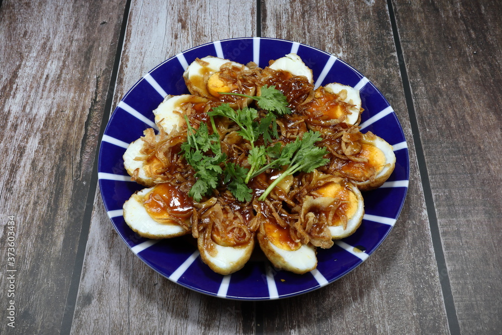 Traditional fried boiled egg with sweet dipping sauce and topping with dried crispy shallot on the plate. Famous royal ancient Thai menu in Asia restaurant. 