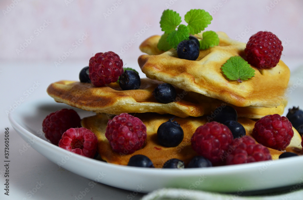 Homemade Belgium Waffles with fresh blueberries for breakfast. White plate, Viennese waffles with raspberries and mint. quick delicious breakfast on white background Homemade Belgium Waffles with fresh blueberries for breakfast. White plate, Viennese waffles with raspberries and mint. quick delicious breakfast on white background