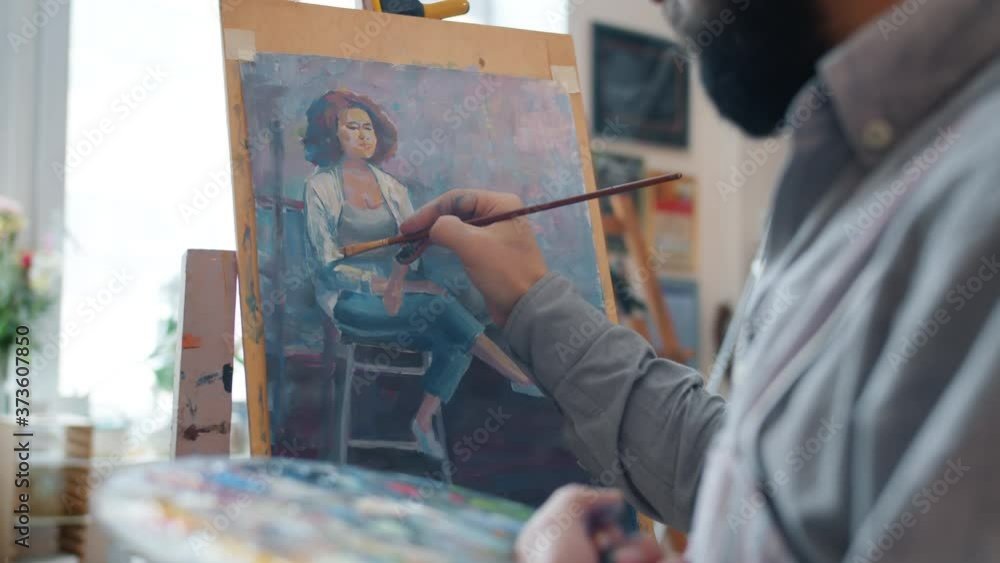 Talented male artist is creating portrait of young woman working indoors in workshop concentrated on colorful picture. Creative people and occupation concept Talented male artist is creating portrait of young woman working indoors in workshop concentrated on colorful picture. Creative people and occupation concept