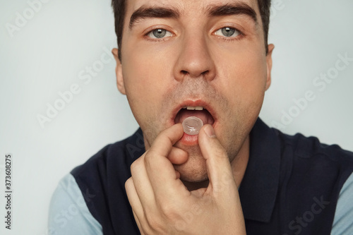 young cute man sucks a pill from inflammation of the tonsils. . man eating pills cough sore throat pastille colorful. a mint for fresh breath photo