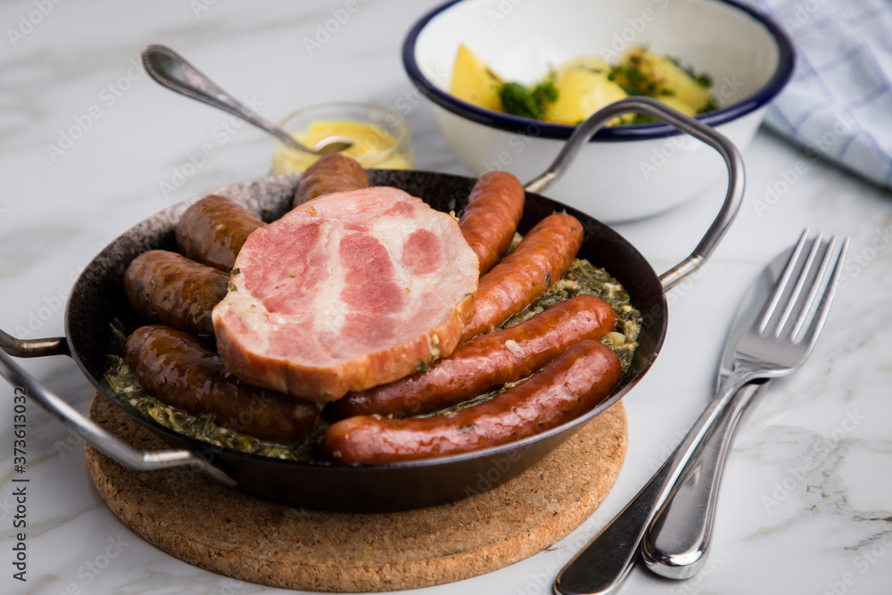 Oldenburger Grünkohl mit Pinkel, Kohlwurst, Kassler Schweine Nacken, Senf und Kartoffeln in Gusseisen Pfanne auf Marmor Tisch Oldenburger Grünkohl mit Pinkel, Kohlwurst, Kassler Schweine Nacken, Senf und Kartoffeln in Gusseisen Pfanne auf Marmor Tisch