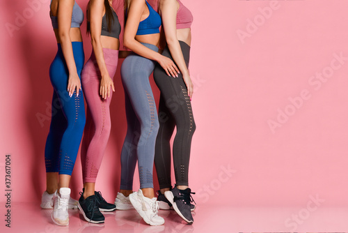 Closeup on legs of standing behind each other athletic women in blue, grey, brown training suits on pink background