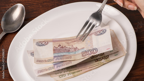 Russian rubles on a white plate. Keep money on the fork. Minimum subsistence level, food basket, minimum wage. Concept. Eat money, living wage. Economy.  Crisis, inflation, business, Finance