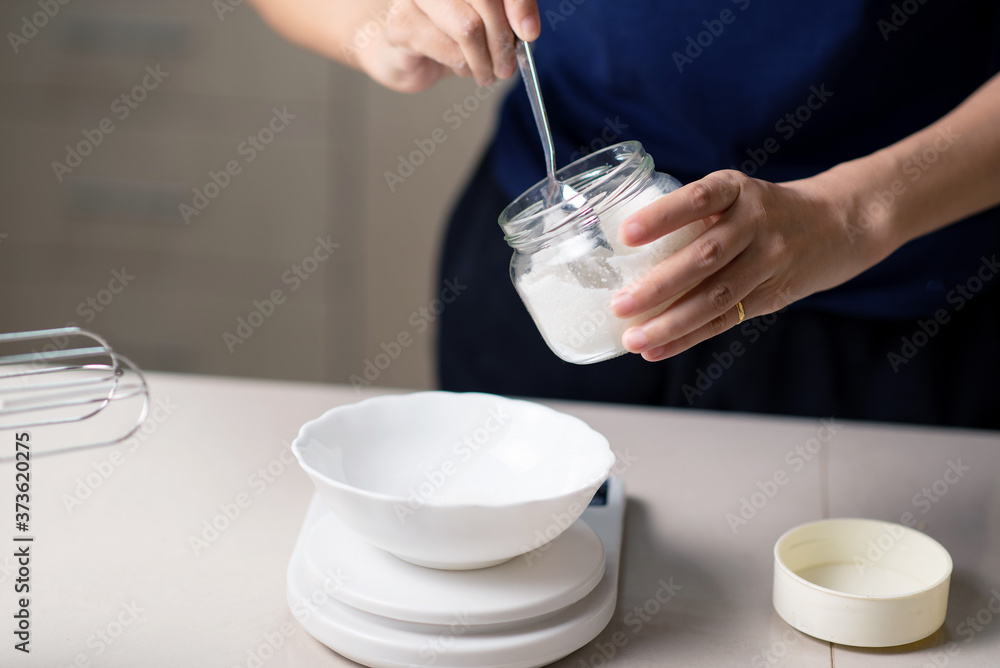 Woman measuring sugar on a small kitchen scale while making cookies Woman measuring sugar on a small kitchen scale while making cookies