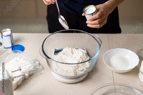 Fotografia Woman adding bicarbonate soda to flour on a small kitchen scale while making coo