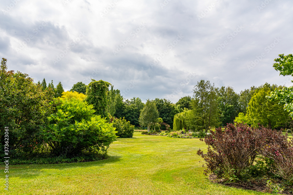 Between the threatening clouds a dim sun illuminates this beautifully landscaped garden with a great diversity of trees and flowering shrubs near the village of Harkstede in Groningen
