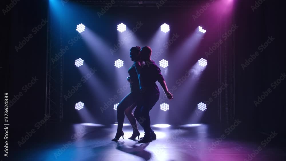 Young couple dancing latin music. Bachata, merengue, salsa. Shot in a dark studio with neon lights in the background. Young couple dancing latin music. Bachata, merengue, salsa. Shot in a dark studio with neon lights in the background.