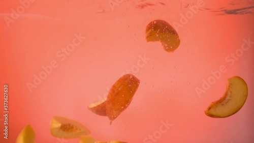 Slices of peaches fall into the water on an orange background. Up close. Slow mo