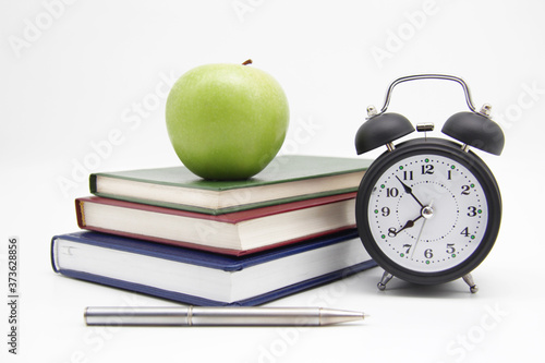 Back to school. Educational concept, office supplies. A stack of books, a green Apple, an alarm clock, and a pen on an isolated white background. A copy of the space.
