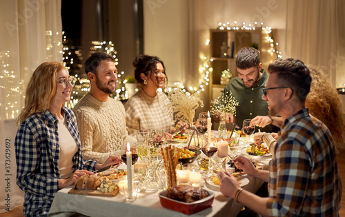 holidays, celebration and people concept - happy smiling friends having christmas dinner party at home in evening