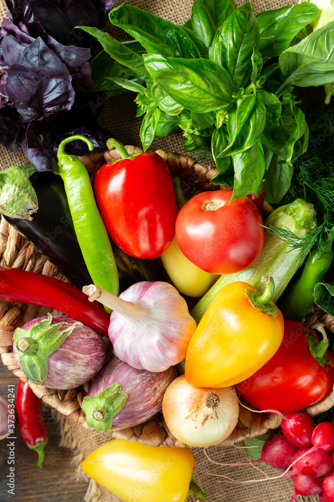 Assortment of vegetables in a basket on the table. A lot of different raw vegetables in the basket. Eggplant, tomatoes, garlic, sweet pepper, onion on the table. The concept of healthy eating