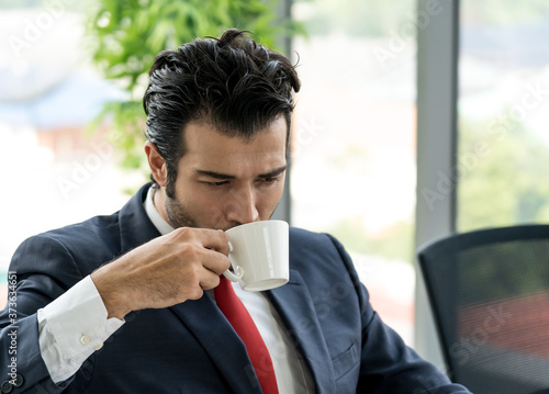 Businessman is sipping cup of coffee while sitting in the office