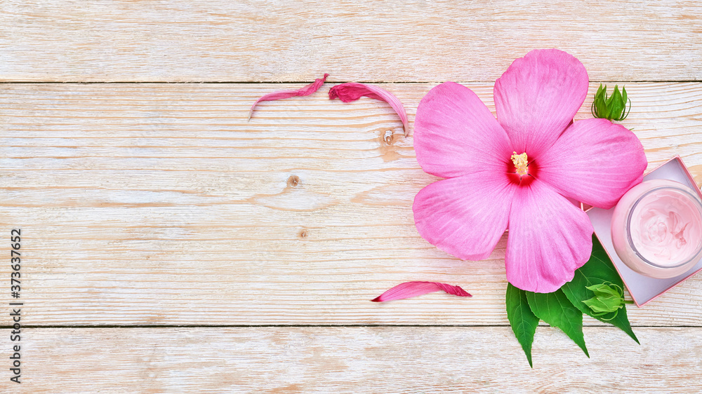 pink hibiscus flower and a jar of cream on a white wooden background. beauty products pink hibiscus flower and a jar of cream on a white wooden background. beauty products